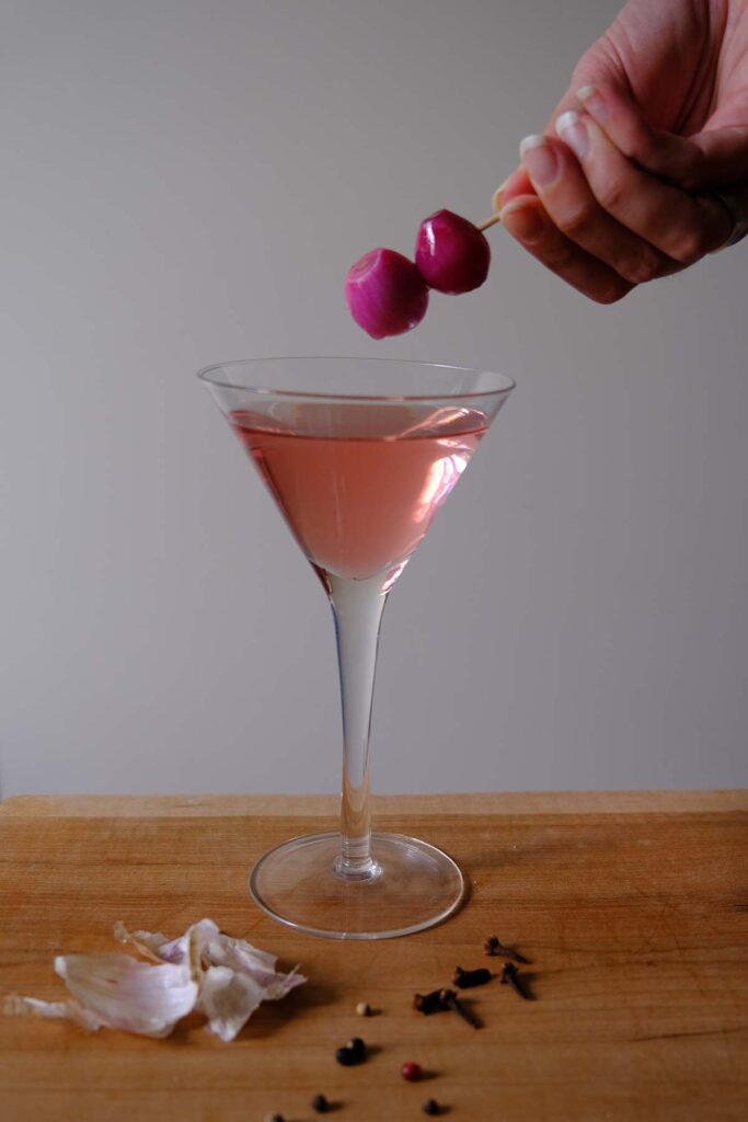 A martini glass with pink Gibson cocktail with the with two cocktail onions on a toothpick