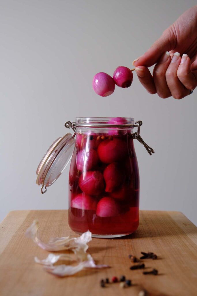 A glass jar with pickled pink cocktail onions and two pickled onions on a toothpick