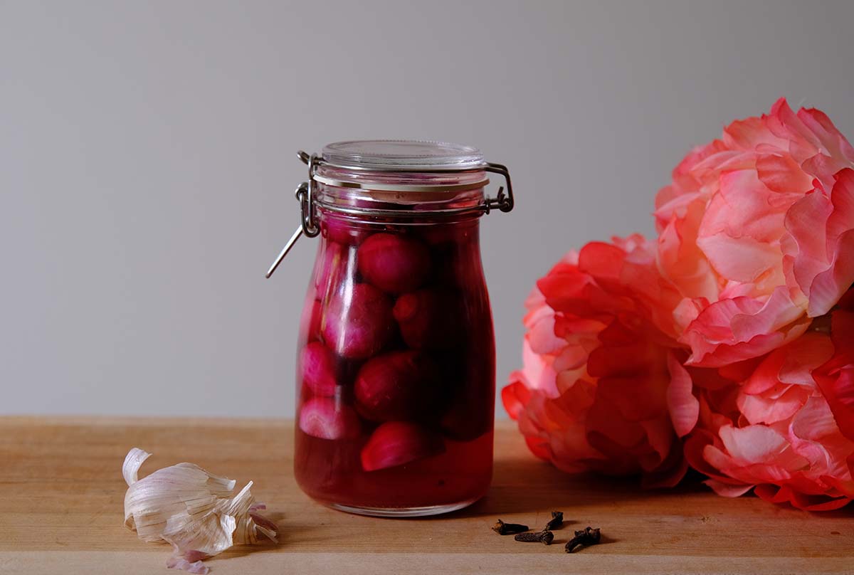 A glass jar with pickled pink cocktail onions and some pink flowers