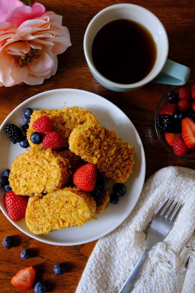 Golden brown French toast slices with cornflakes, served with blackberries, strawberries, and coffee.