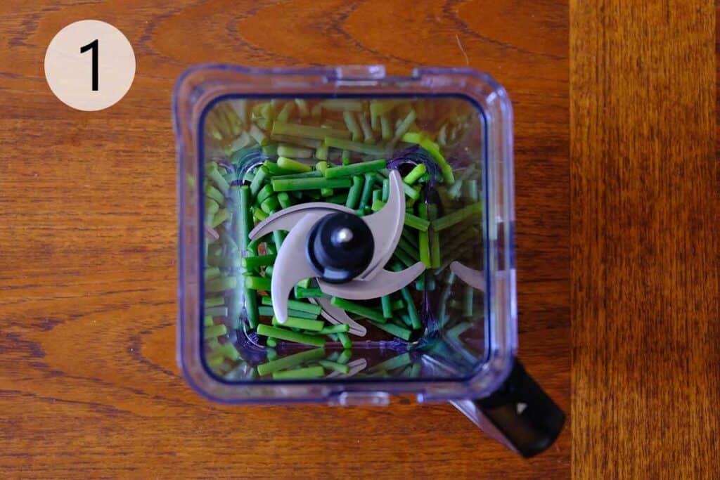 Steps to make this garlic scape pesto recipe - Chopped garlic scapes in a food processor, ready to be pulsed for pesto