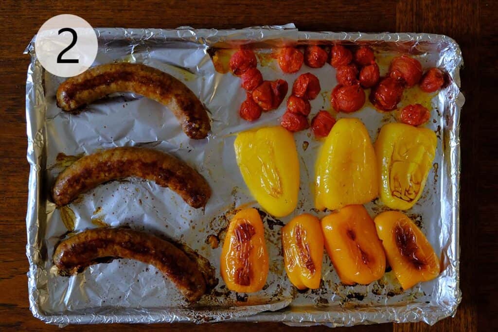 Roasted bell peppers, cherry tomatoes, and sausage on a baking tray fresh from the oven, caramelized and golden around the edges.