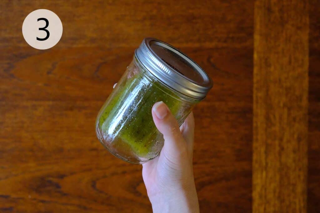 Homemade Italian dressing ingredients—olive oil, vinegar, sugar, oregano, and basil—being mixed in a mason jar for pasta salad