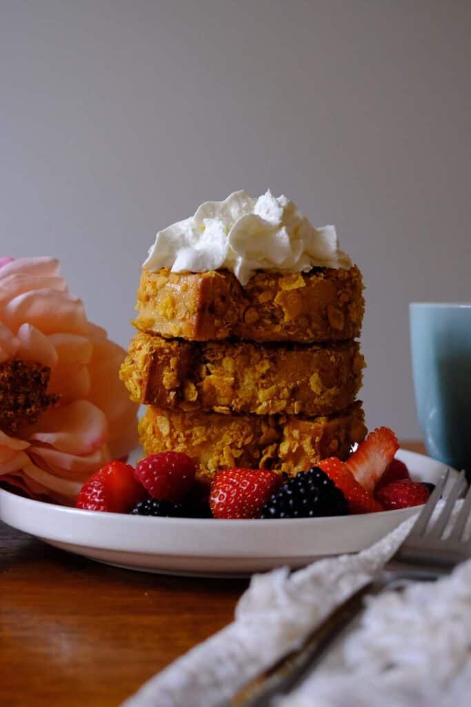 Cornflake-coated French toast slices stacked high, topped with whipped cream and served with berries.