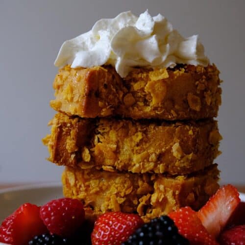 Stack of crispy cornflake French toast with whipped cream and fresh berries — a golden brunch treat.