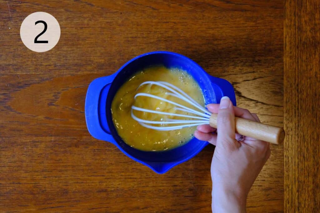 Preparing the egg custard for Crispy French Toast in a blue bowl on a wooden table