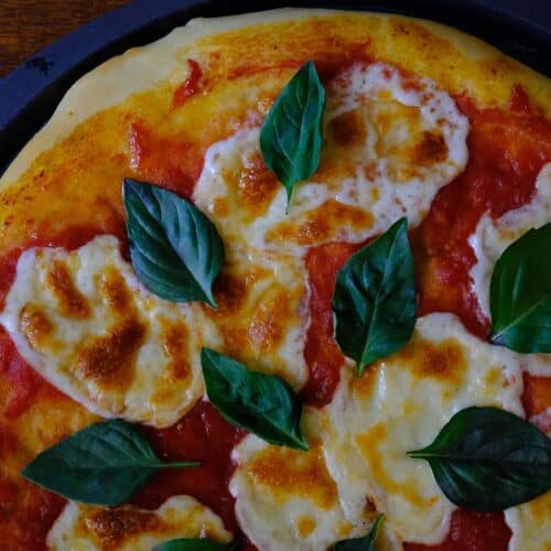 Authentic Margherita pizza on a wooden table with fresh basil, bubbly mozzarella