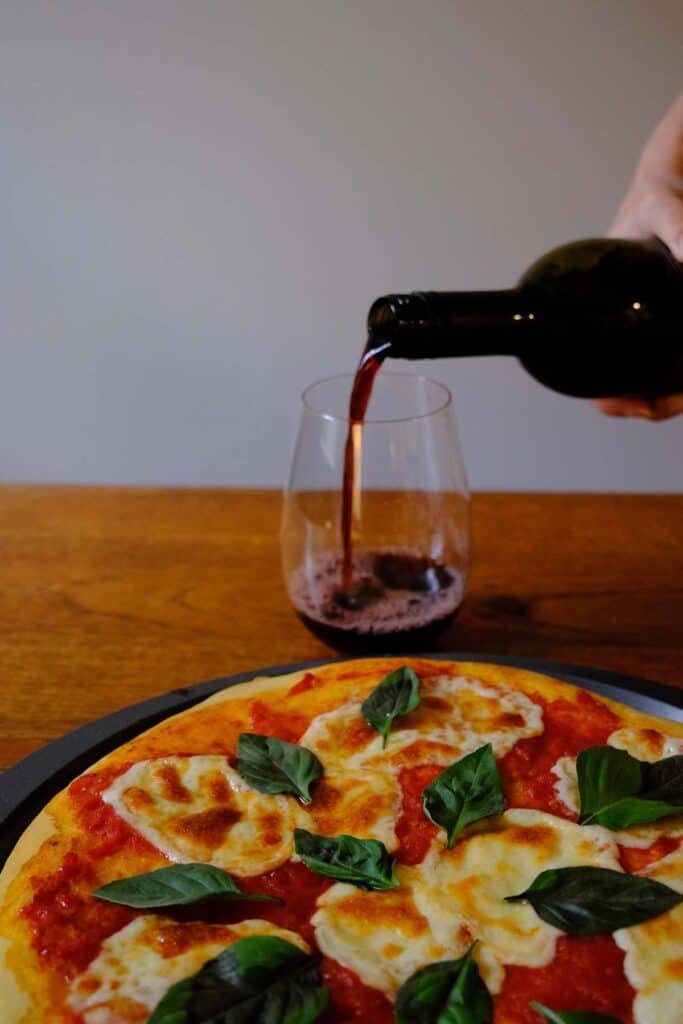 Classic Neapolitan-style Margherita pizza served with wine on rustic wood table