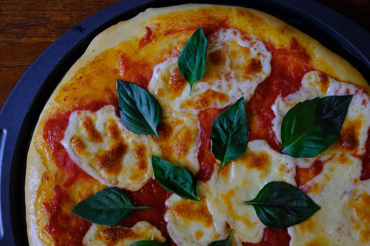 Authentic Margherita pizza on a wooden table with fresh basil, bubbly mozzarella