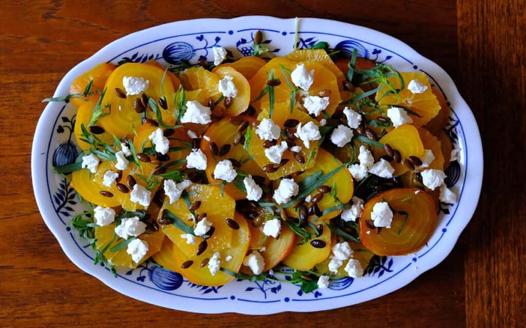 Vibrant golden beet salad recipe featuring sliced beets, citrus, goat cheese, and tarragon on a serving dish.