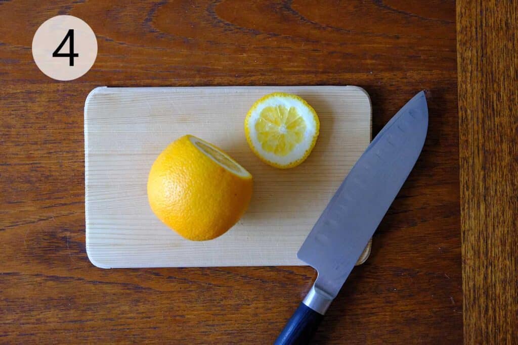 Fresh navel oranges being sliced into rounds with a chef’s knife, displayed on a cutting board on a wooden surface.