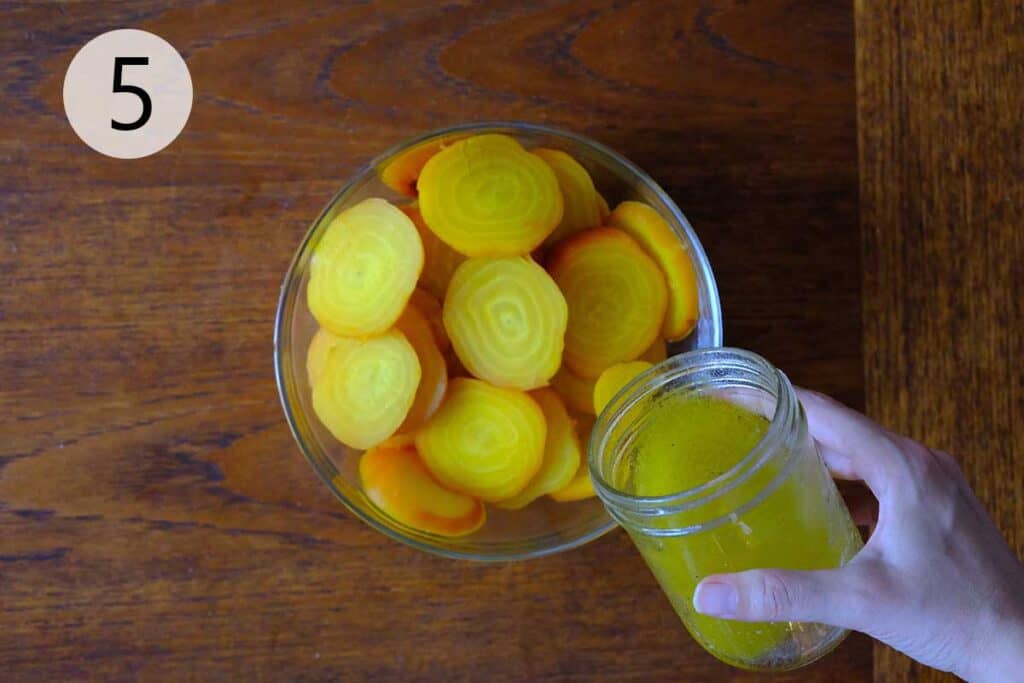Cooked golden beets with skins rubbed off, sliced into rounds and placed in a bowl with orange slices about to be dressed with salad dressing.