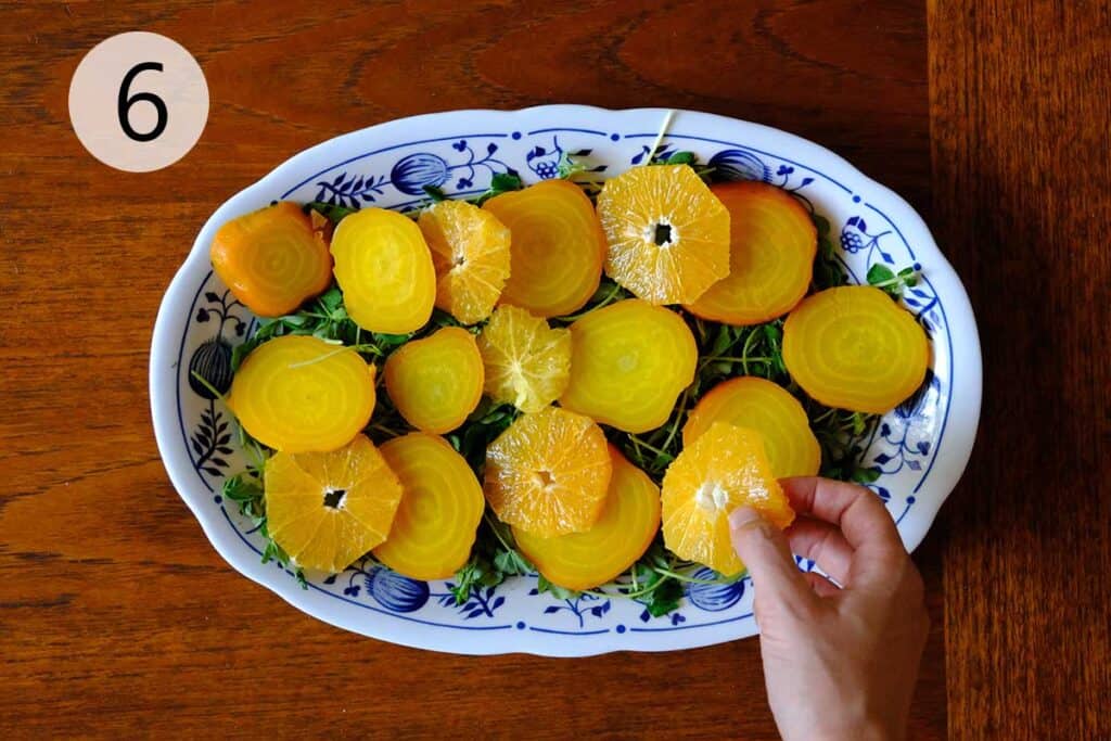 Golden beet and citrus salad being arranged on a platter with greens shot from overhead.