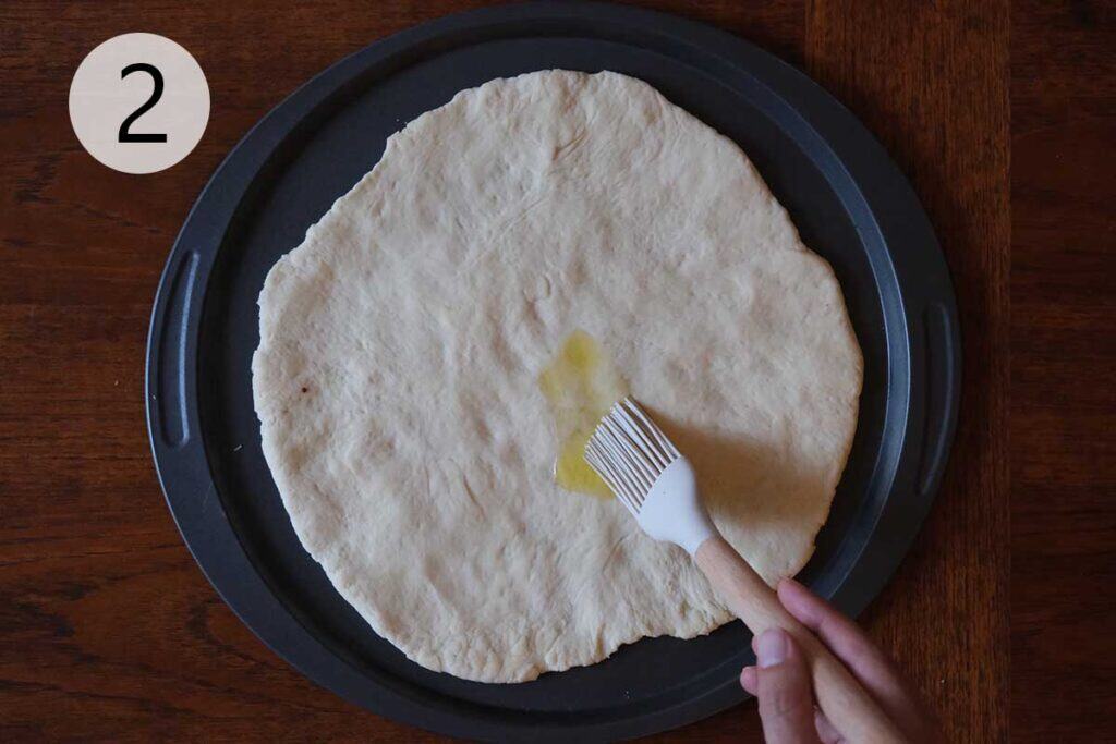 Instructions to make this pear pizza recipe - step two stretching the pizza dough and brushing it with olive oil