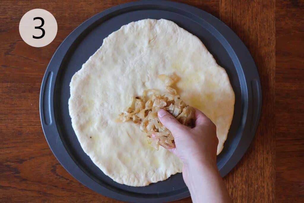 Instructions to make this pear pizza recipe - step three covering pizza dough in caramelized onions