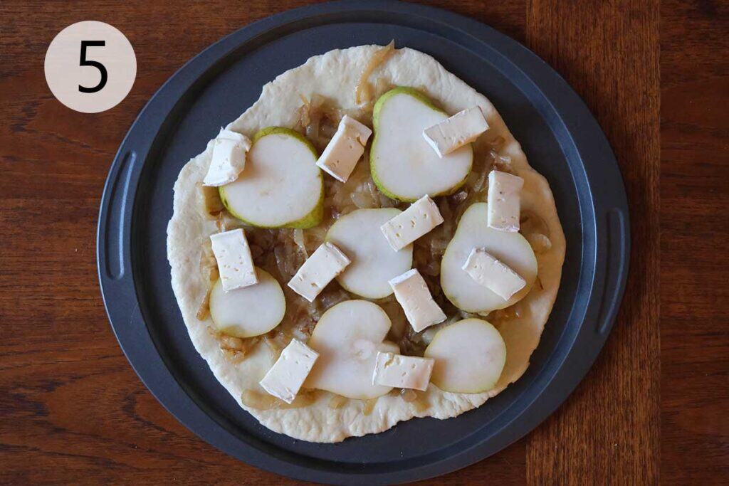 Instructions to make this pear pizza recipe - step four topping the pizza with pieces of sliced brie