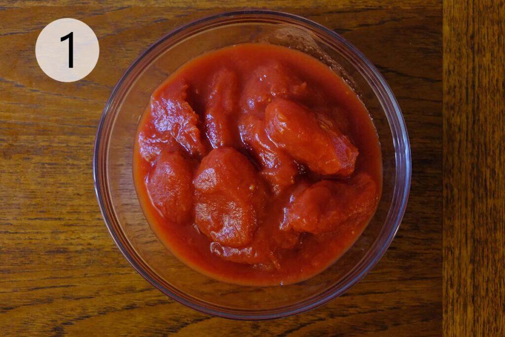 San Marzano tomatoes in a bowl being mixed by hand to make simple pizza sauce