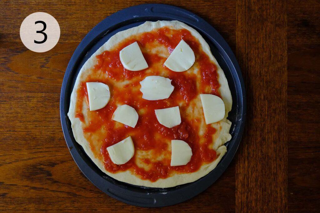 Fresh mozzarella slices and tomato sauce being layered onto shaped pizza dough before baking