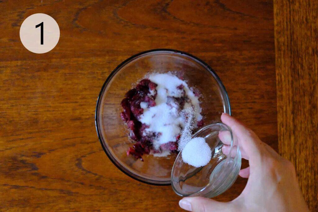 Mashed cherries sprinkled with sugar in a bowl, releasing juice to start the homemade Luxardo cherry recipe.