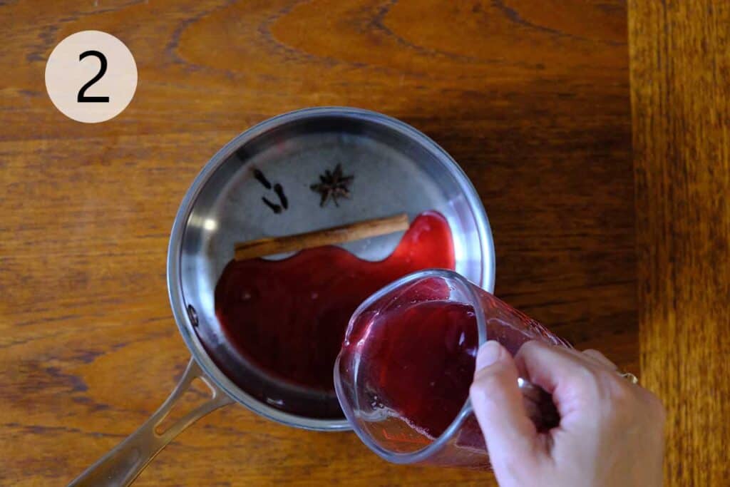 Raw sugar, cherry juice, and whole spices simmering in a saucepan to create a rich spiced syrup.