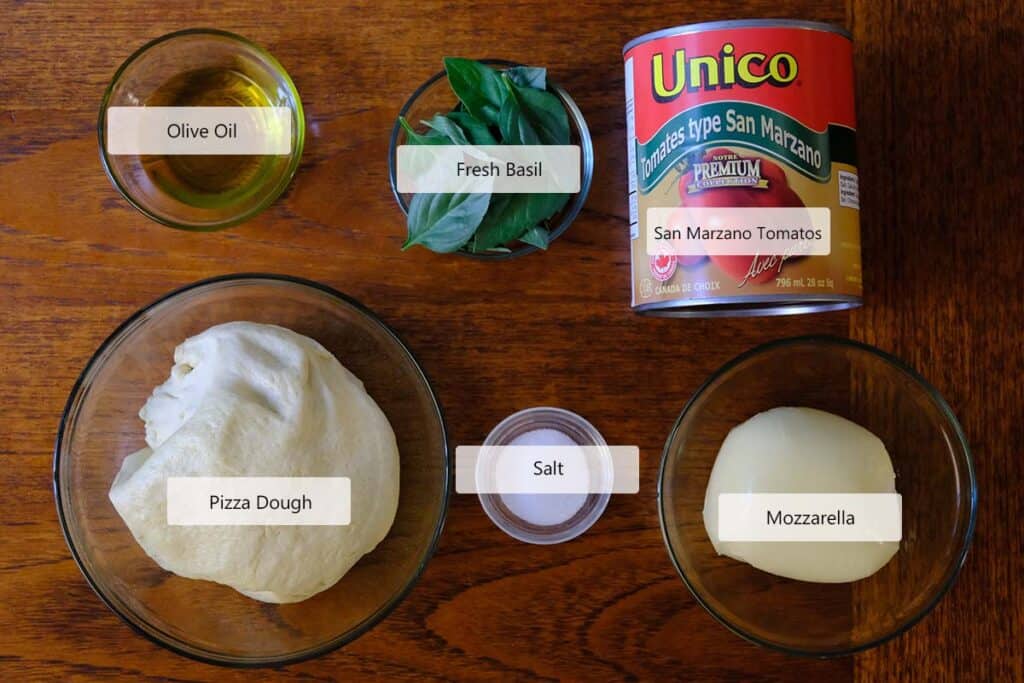 Ingredients for authentic Margherita pizza laid out on a wooden table, including pizza dough, San Marzano tomatoes, mozzarella, fresh basil, olive oil, and salt