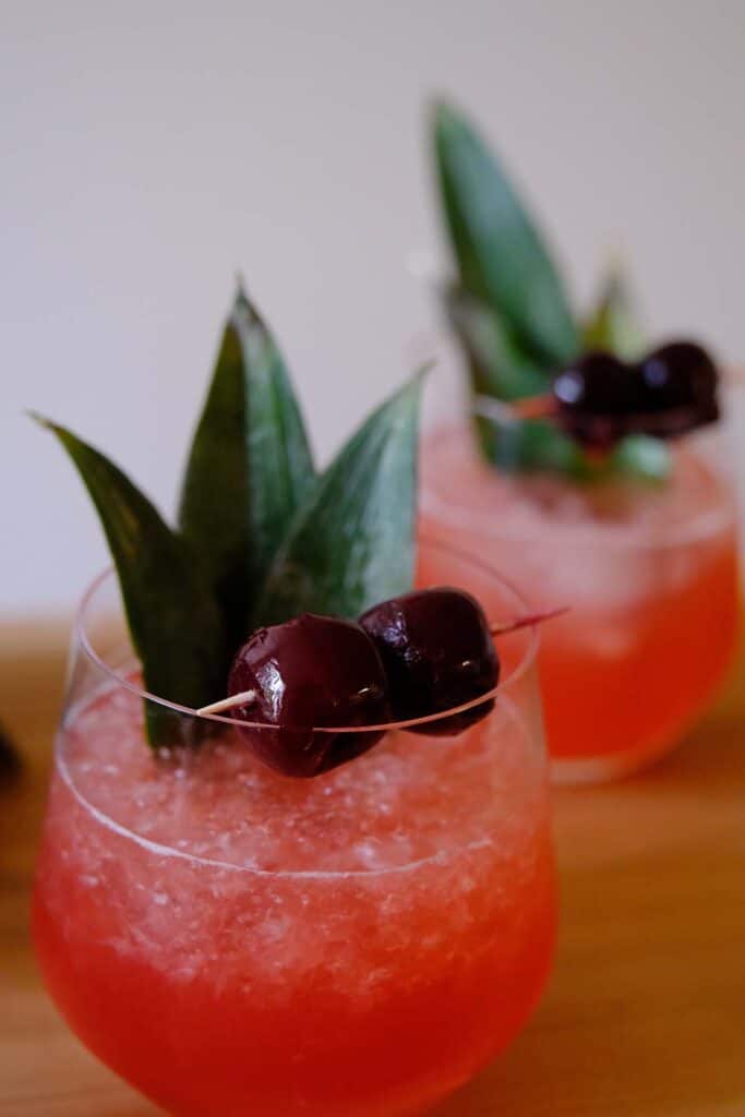Refreshing Shark's Tooth Cocktail featuring tiki garnishes like pineapple fronds and cocktail cherries for a classic presentation.