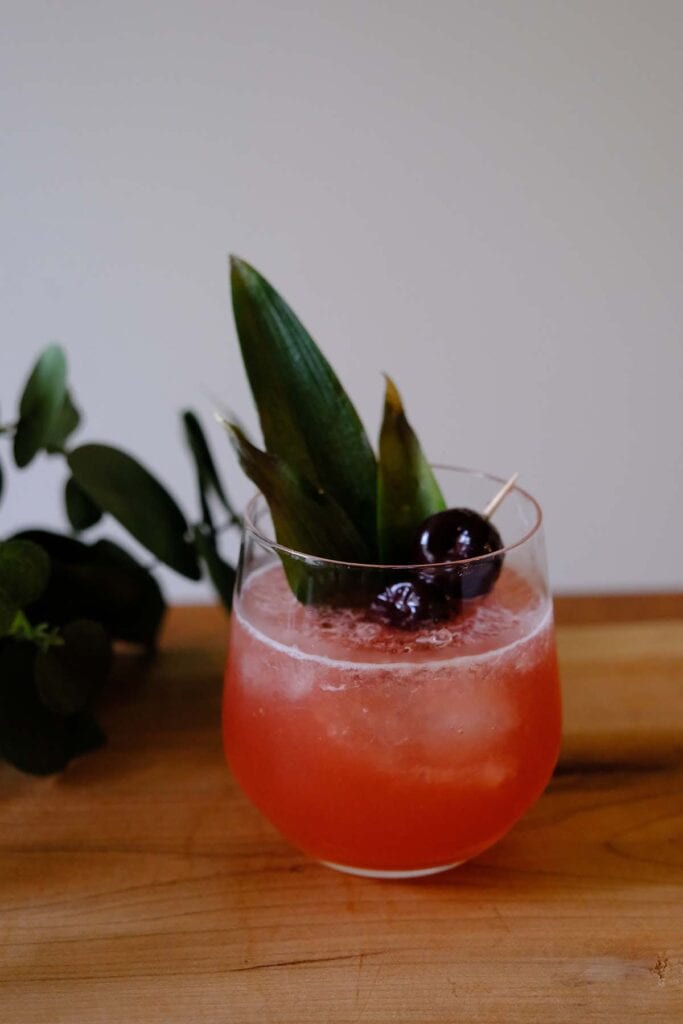 Shark's Tooth Cocktail with Luxardo cherries and pineapple leaves for a bold Tiki-style finish.