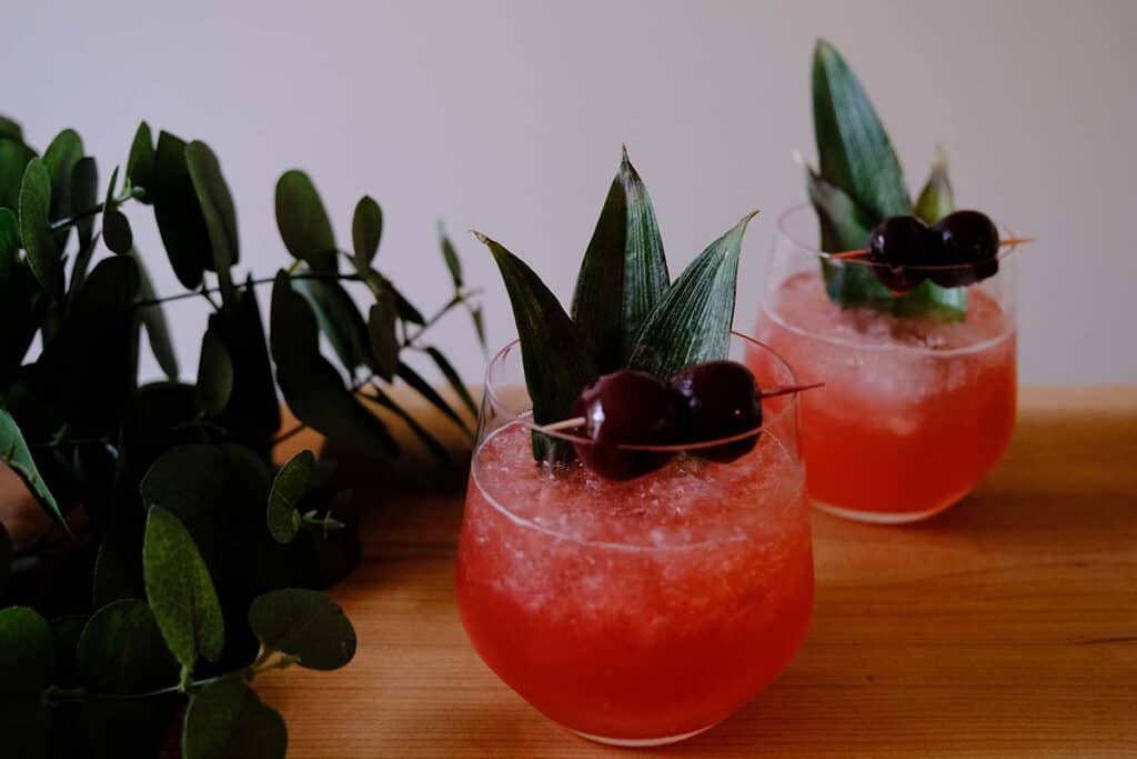 Finished Shark's Tooth Cocktail with crushed ice, pineapple leaf garnish, and Luxardo cherries for a tropical Tiki presentation.
