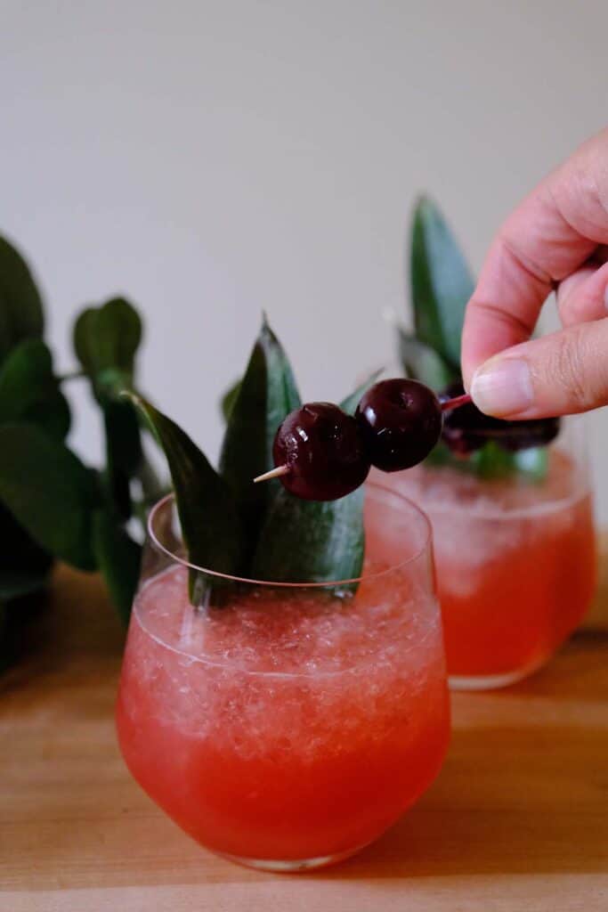 Garnishing a Shark's Tooth Cocktail with Luxardo cherries and pineapple leaves for a bold Tiki-style finish.