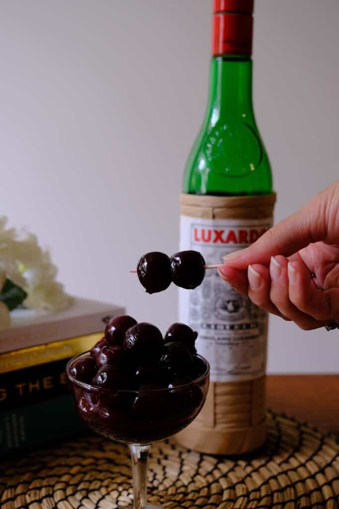 Close-up of homemade Luxardo cherry recipe served in a coupe glass, with Luxardo liqueur bottle in soft focus.