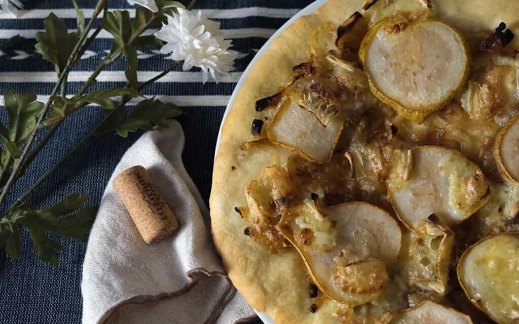 Close-up of homemade pear pizza with caramelized onions and brie on a white plate – perfect for a fall or gourmet pizza night.
