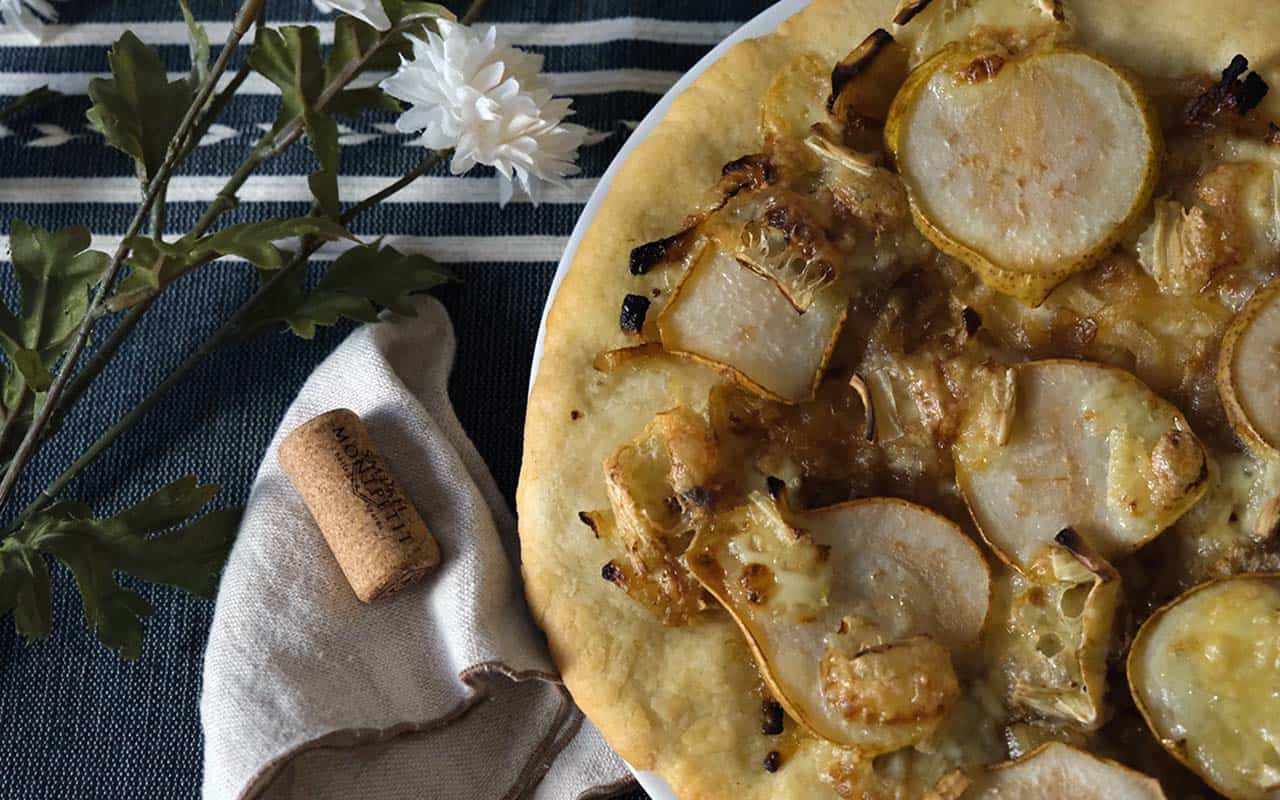 Close-up of homemade pear pizza with caramelized onions and brie on a white plate – perfect for a fall or gourmet pizza night.