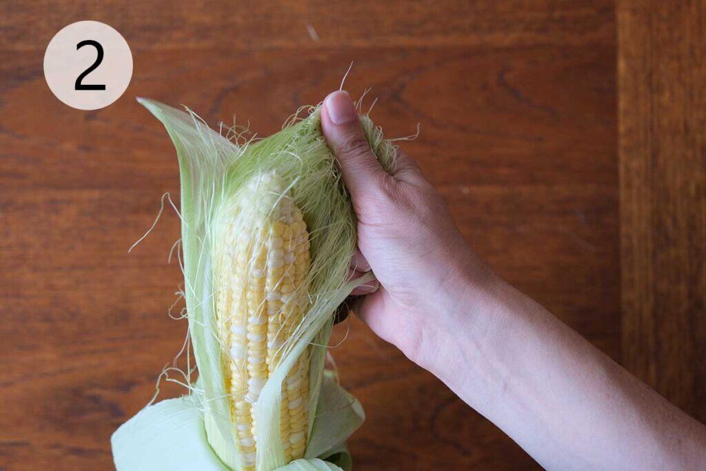 Corn on the cob with husks partially peeled, ready for the grill.