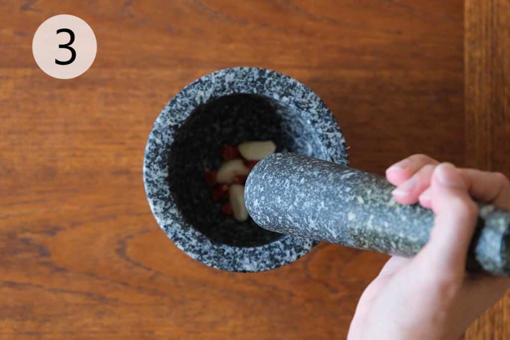 Pounding garlic and Thai chilies in a mortar and pestle for salad dressing.
