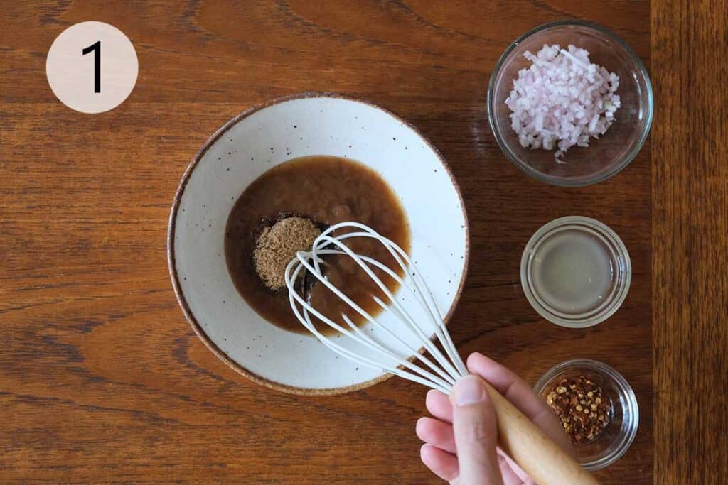 Mixing tamarind paste, fish sauce, lime juice, brown sugar, chili flakes, and shallots in a bowl to make the base of Nam Jim Jeaw Thai dipping sauce.