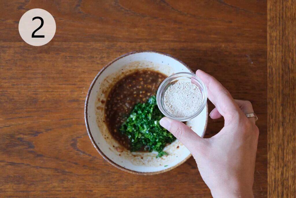 Stirring in fresh cilantro, green onions, and toasted rice powder (Khao Khua) to finish a Thai dipping sauce recipe Nam Jim Jeaw