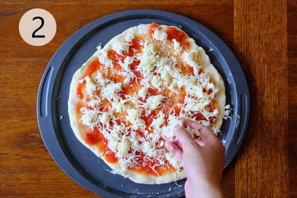 Sprinkling freshly grated mozzarella overtop of Tomato Sauce.