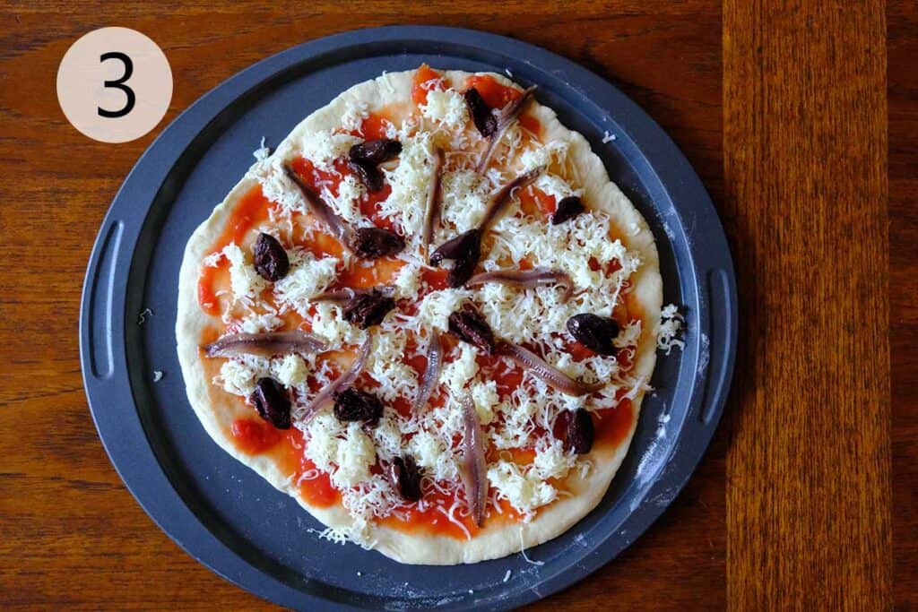 An pizza with salty anchovies, briny olives and chili flakes ready to be baked.