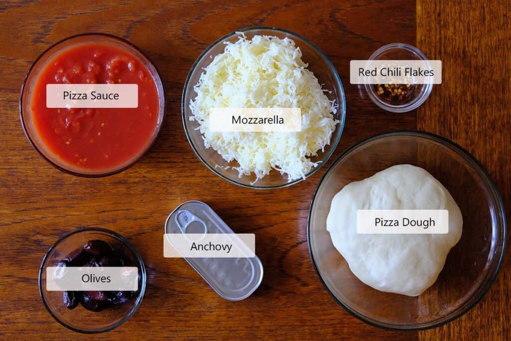The ingredients to make this homemade Anchovy Pizza Recipe prepped on a wooden table