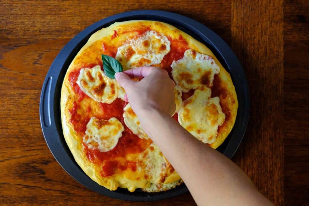 placing fresh basil on top of a freshly baked margarita pizza made with authentic Neapolitan pizza sauce