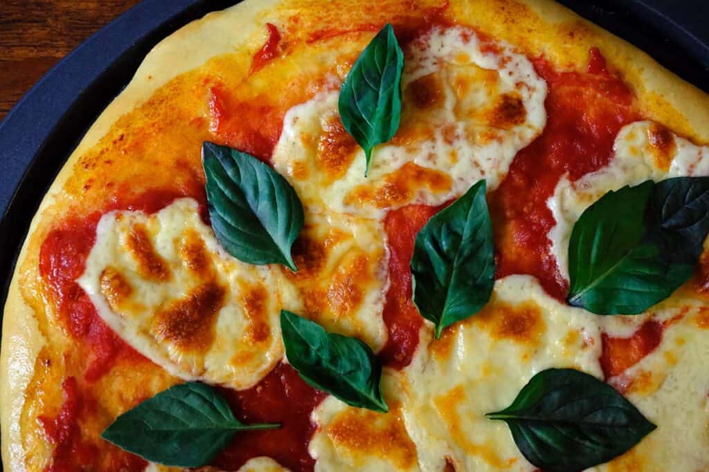 Top down view of a margarita pizza with fresh basil and lightly browned mozzarella