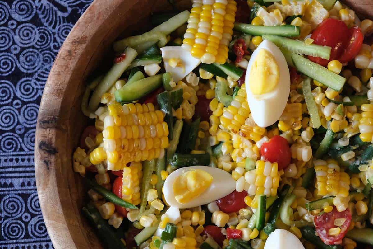 Close-up of Thai spicy corn salad with salted duck eggs, crunchy green beans, cucumbers, and cherry tomatoes, perfect with sticky rice and other Thai cuisines