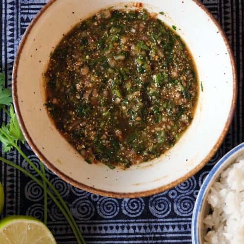 Flat lay of Nam Jim Jeaw, a Thai dipping sauce made with tamarind, fish sauce, chili, herbs, and toasted rice powder, paired with rice and lime.