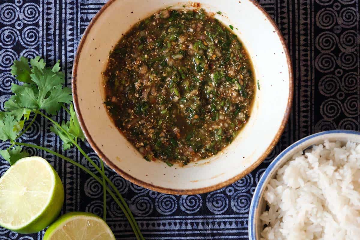 Flat lay of Nam Jim Jeaw, a Thai dipping sauce made with tamarind, fish sauce, chili, herbs, and toasted rice powder, paired with rice and lime.