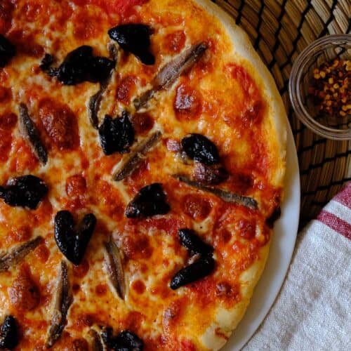 Classic homemade anchovy pizza with black olives and melted mozzarella on a golden pizza crust, perfect for pizza night.