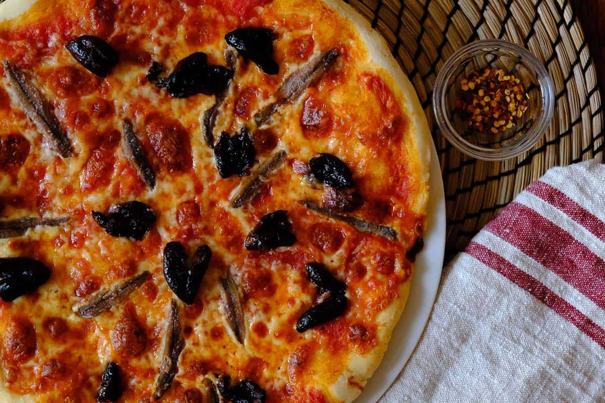 Classic homemade anchovy pizza with black olives and melted mozzarella on a golden pizza crust, perfect for pizza night.