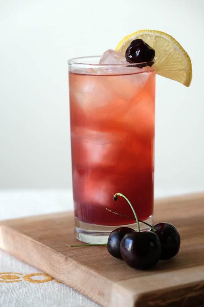 Refreshing Cherry Collins cocktail made with gin, lemon juice, and cherry syrup served in a Collins glass with fresh fruit garnish.