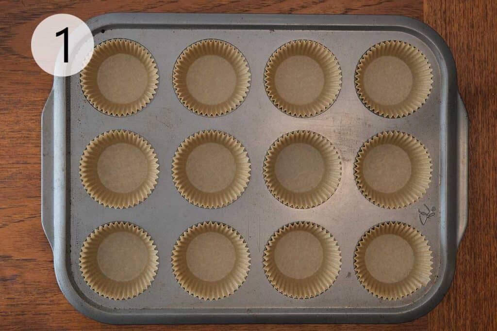 Muffin tin lined with parchment paper liners, ready to bake zucchini and orange muffins.