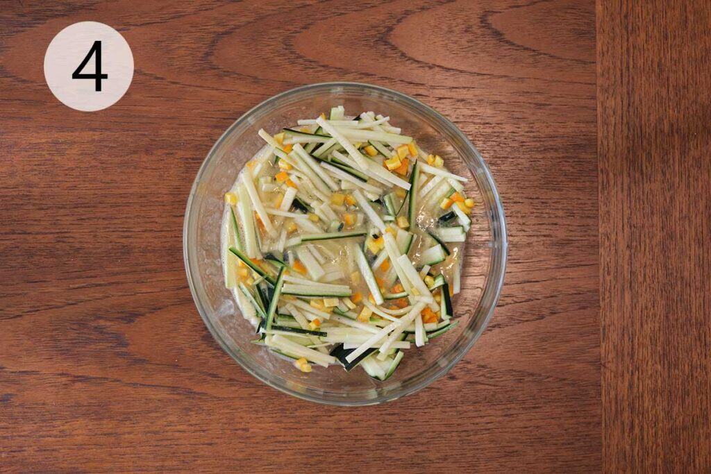 Bowl of wet ingredients with zucchini and orange zest being combined before adding to the dry mixture.
