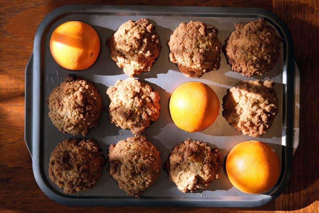 Homemade zucchini and orange muffins with walnut crumb topping in a muffin tin.